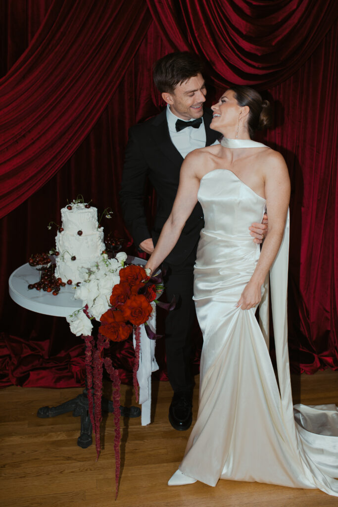 Emily and Patrick embracing during red draped editorial wedding shoot