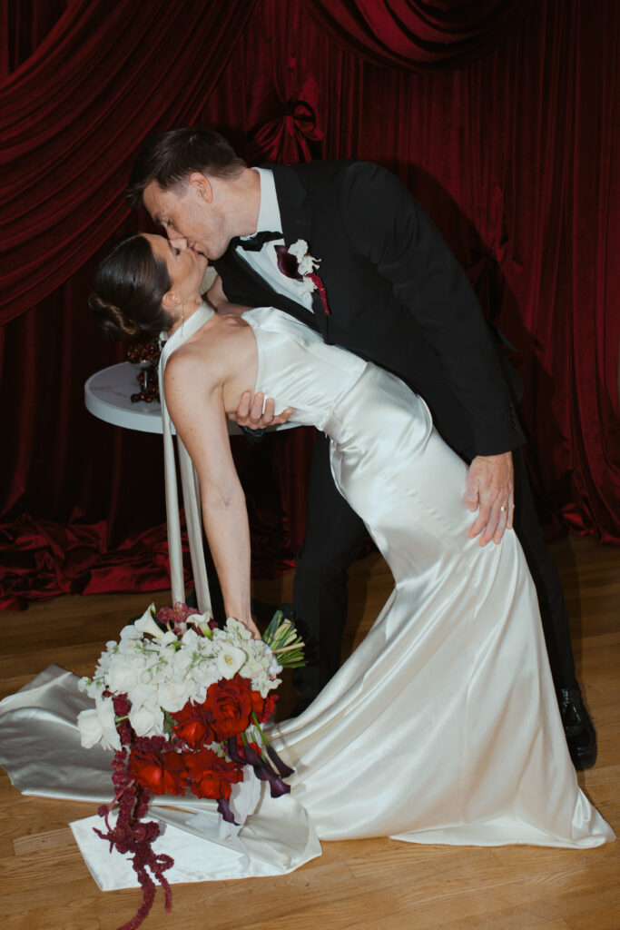 Emily and Patrick embracing during red draped editorial wedding shoot