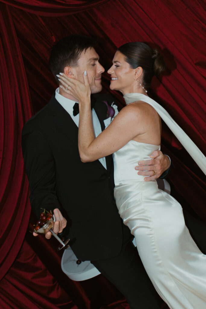 Emily and Patrick embracing during red draped editorial wedding shoot